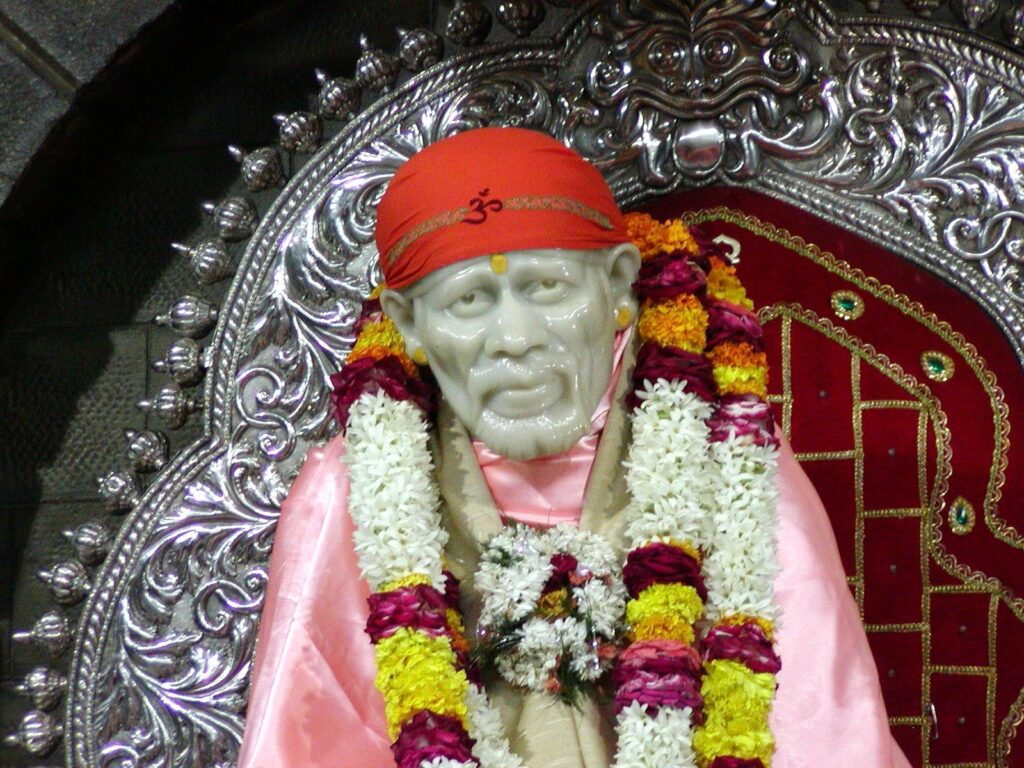 Statue of Sai Baba adorned with garlands and a red headscarf.