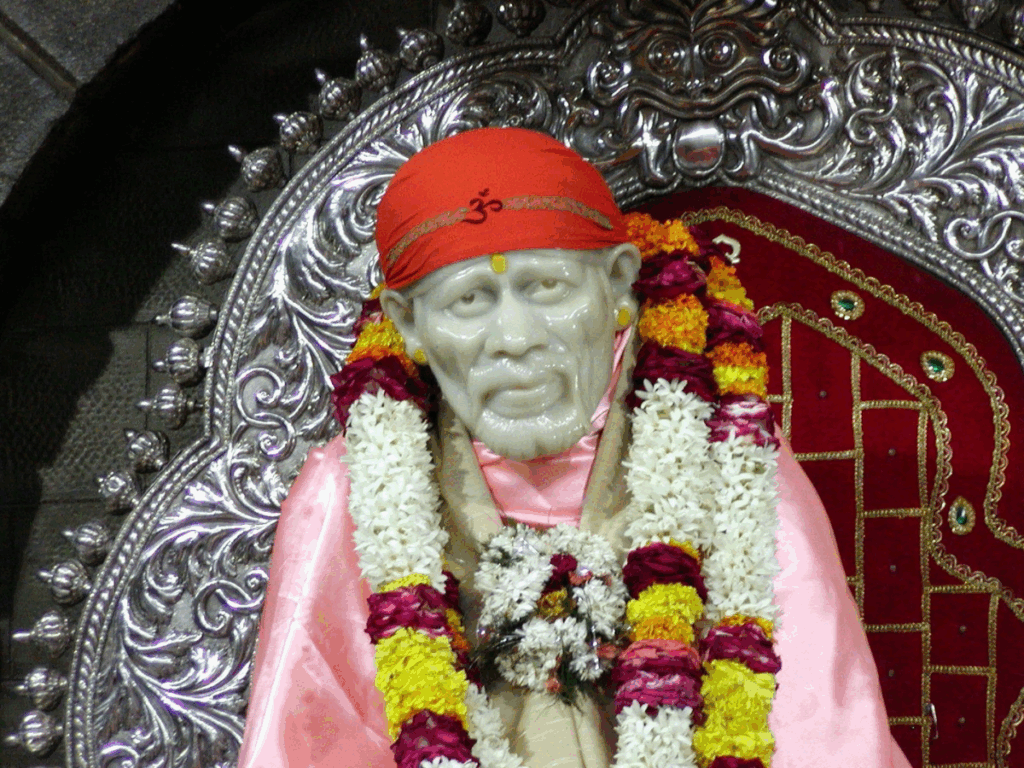 Statue of Sai Baba adorned with garlands and a red headscarf.